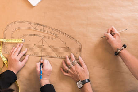 Overhead view of seamstresses hands drawing with curved ruler on dressmakers pattern in workshop