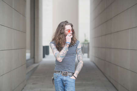 Young male hippy smoking cigarette in city alleyの写真素材