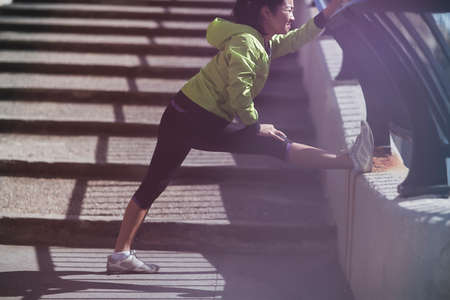 Young woman standing on outdoor steps, doing stretchesの写真素材