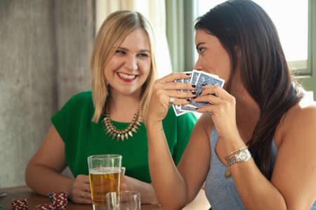 Two female friends playing cards, and laughing, at tableの写真素材