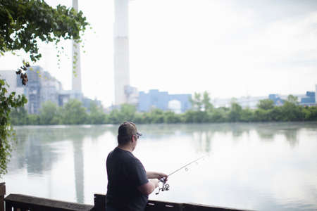Man fishing opposite Detroit Edison Power Station, river Raisin, Monroe, Michigan, USA