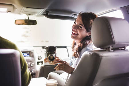 Over shoulder view of young woman in car front seat with SLR cameraの写真素材