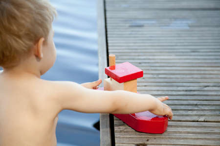 Rear view of male toddler playing with toy boat on pierの写真素材