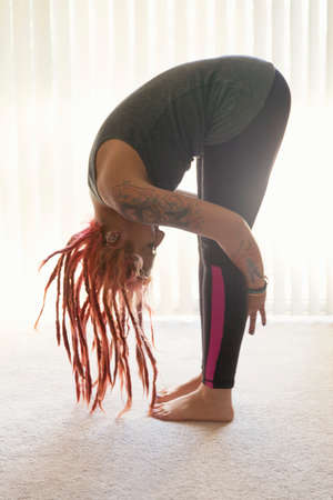 Young woman with pink dreadlocks practicing yoga in living roomの写真素材