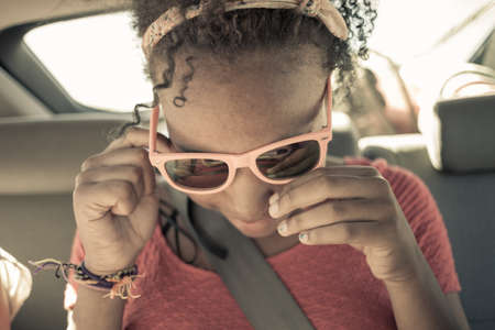 Close up of girl peering though sunglasses on car back seatの写真素材