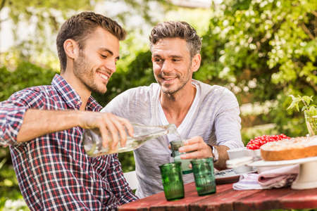 Two male friends having drink together at table in gardenの写真素材