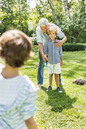 Mature man teaching grandsons badminton in gardenの写真素材