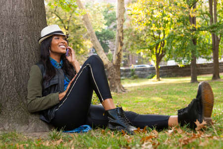 Young woman sitting against tree using smartphone