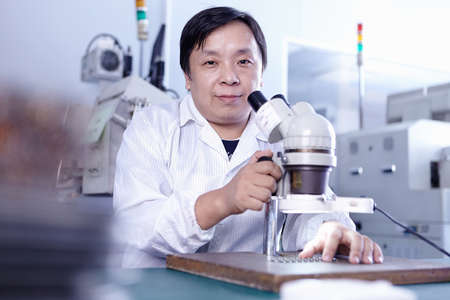 Technician with microscope in LED factoryの写真素材