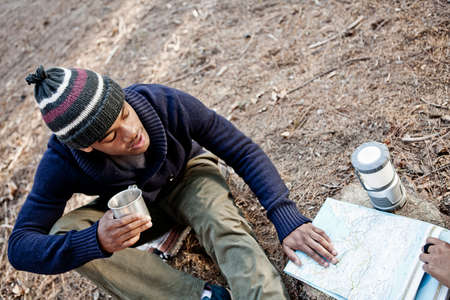 Young man with mug, looking at map outdoorsの写真素材