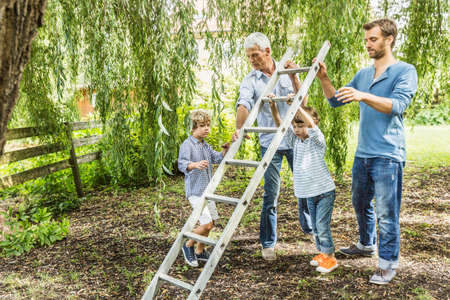 Mature man with son lifting ladder with grandsons in gardenの写真素材
