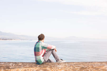 Young man looking at view across the waterの写真素材