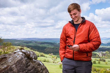 Male teenage hiker reading smartphone texts on top of Guise Cliff, Pateley Bridge, Nidderdale,...