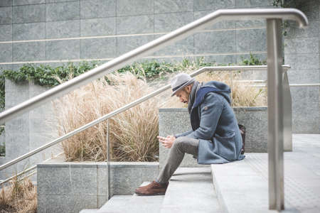 Businessman sitting on stairway texting on smartphoneの写真素材