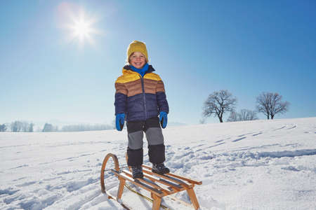 Portrait of young boy standing on sled in snowy landscape