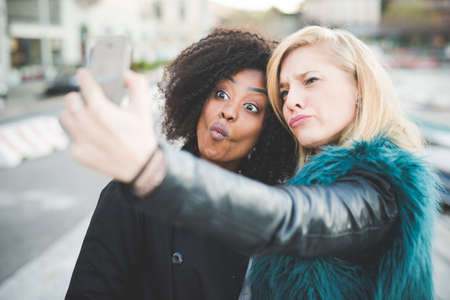 Two young women pulling faces for smartphone selfie, Lake Como, Como, Italyの写真素材