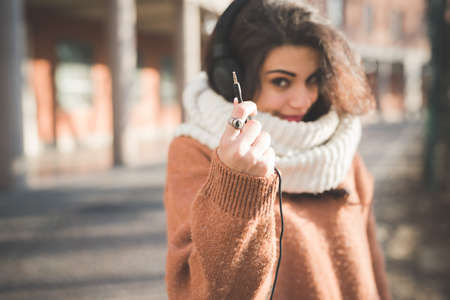Young woman holding up headphone cable on street