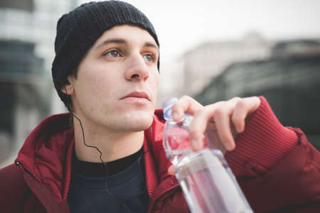 Close up of young man drinking water in city