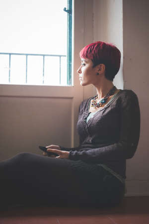 Young woman sitting by window, holding smartphoneの写真素材