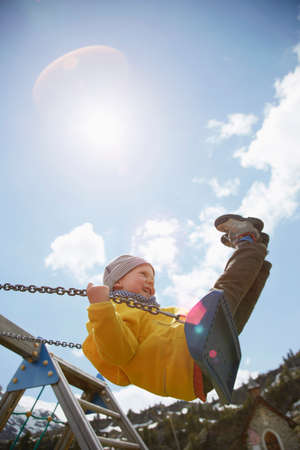 Young boy swinging high on playground swingの写真素材