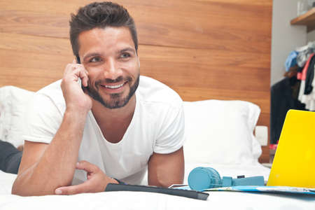 Man lying on bed using phoneの写真素材