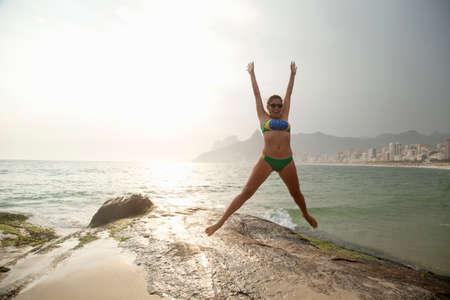 Young woman wearing bikini jumping mid air on  Ipanema beach, Rio De Janeiro, Brazil