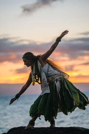Woman hula dancing on coastal rocks wearing traditional costume at sunset, Maui, Hawaii, USAの写真素材
