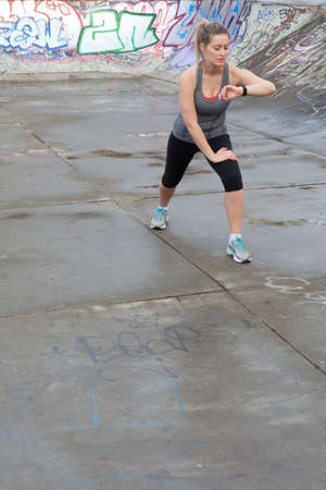 Young female runner warming up and checking stop watch in skateparkの写真素材