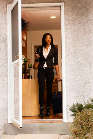 Young woman leaving house with luggageの写真素材