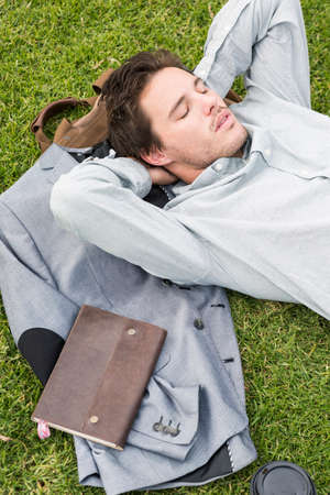 Businessman sleeping on grass, high angleの写真素材