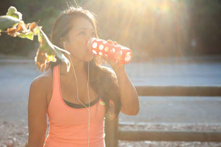 MId adult woman standing by lake, wearing earphones, drinking from water bottle