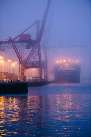 Misty view of cargo ship and cranes on waterfront at night, Seattle, Washington, USAの写真素材