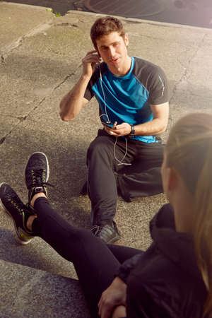 Young male and female runners chatting and listening to earphones