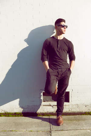 Young man standing by white wall