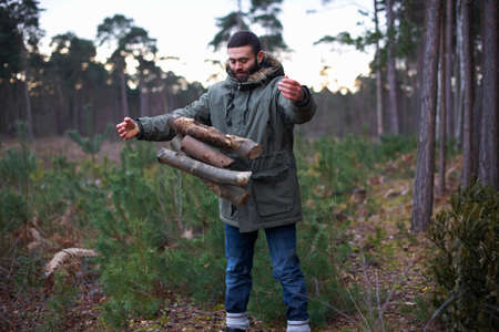 Young man dropping logs for campfire in forest