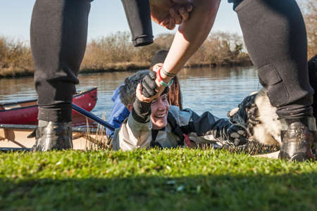 Person helping mid adult woman out from lakeの写真素材