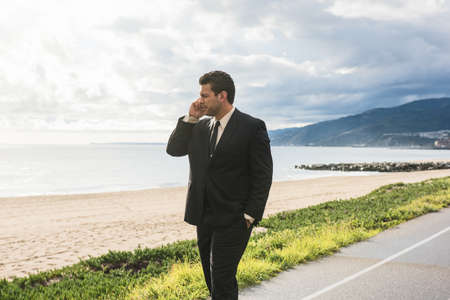 Businessman looking out from coastal highway talking on smartphoneの写真素材