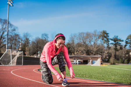 Young female athlete tying trainer laces on track