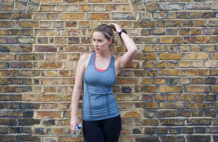 Young female runner leaning against brick wall taking a breakの写真素材