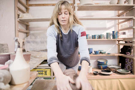 Female potter throwing and rolling clay on workbench