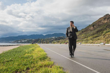 Businessman strolling on coastal highway talking on smartphone