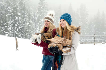 Two young female friends carrying logs in snowy mistの写真素材