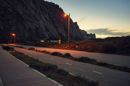 Silhouetted view of Morro Bay Rock and coast road at dusk, Morro Bay, California, USA