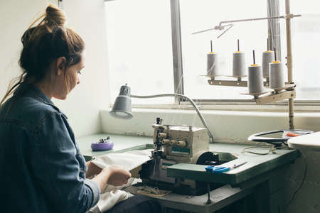 Young female seamstress sewing textile on sewing machineの写真素材