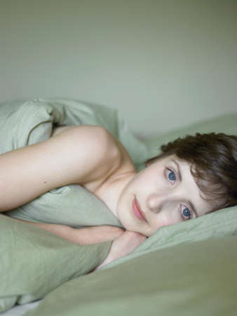 Portrait of beautiful young woman lying in bed wrapped in duvet