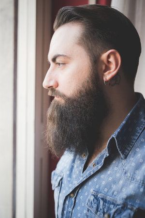Young bearded man looking out of windowの写真素材
