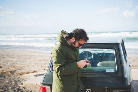 Man with vintage car on beach reading smartphone texts, Sorso, Sassari, Sardinia, Italy