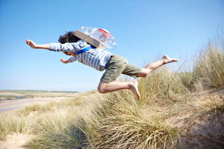 Young boy on beach, wearing fancy dress, leaping into air