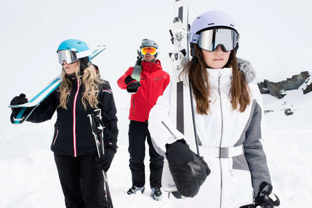 Friends wearing helmets and ski goggles holding skis, portrait