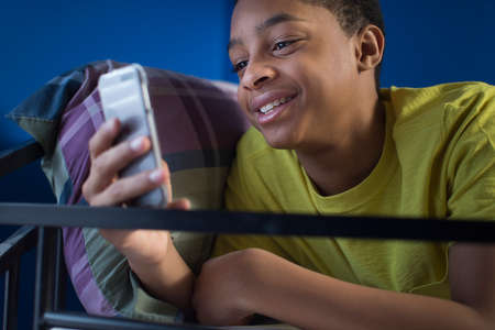 Close up of teenage boy lying in bunkbed reading smartphone text